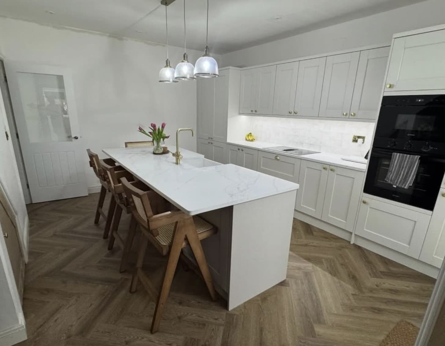 Light grey shaker kitchen with a marble waterfall island, brass tap and herringbone floor by Cunningham & Co